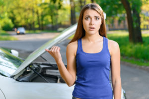 Девушка, указывая на автомобиль с открытым капотом
